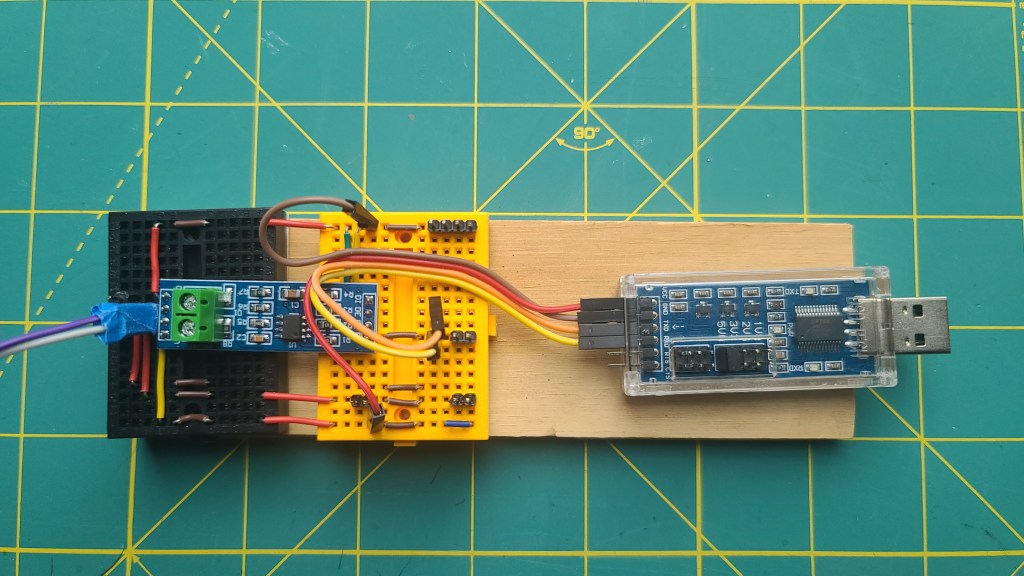 Photo of a test harness built with solderless bread boards, RS485 transceiver, and USB UART device. The test rig is mounted on small sheet of plywood about 2" x 7"