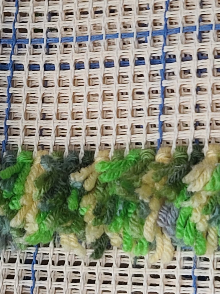 The first few rows of a latch hook rug, showing some exposed canvas.
